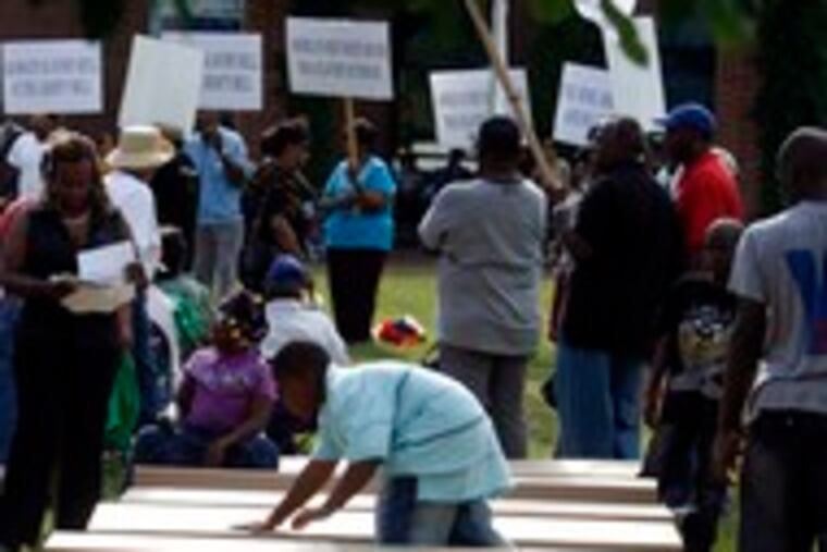 Nine cardboard coffins representing George Washington's slaves in Philadelphia are prepared at Sixth and Market Streets across from the President's House excavation. The event, which drew about 200 people, featured eulogies read by children and a release of balloons.