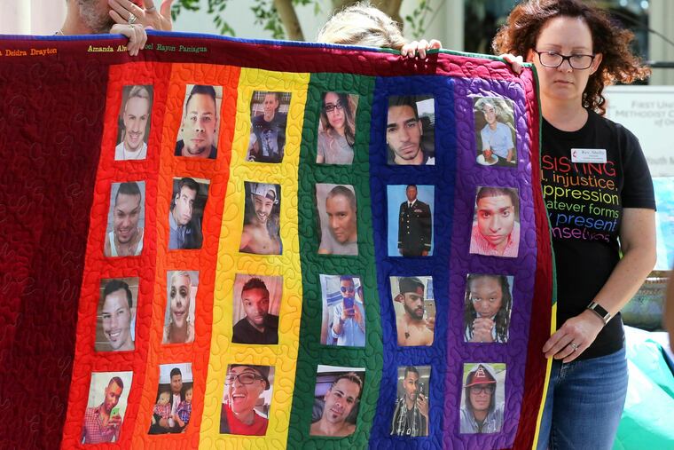 Douglas Barrett, left, and Rev. Shelly Denmark, with others, hold a memorial quilt during the tolling of the bells and reading of the names at First United Methodist Church in Orlando, Fla., Wednesday, June 12, 2019, on the 3rd anniversary of the Pulse nightclub massacre. (Joe Burbank/Orlando Sentinel via AP)