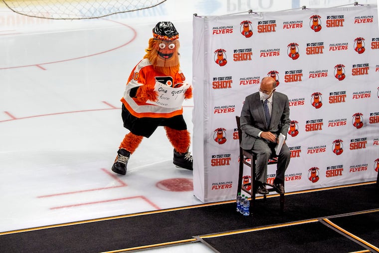 Gritty sneaks up behind Gov. Tom Wolf on the ice at the Wells Fargo Center on Monday to highlight the "Take Your Shot" campaign to encourage vaccinations.