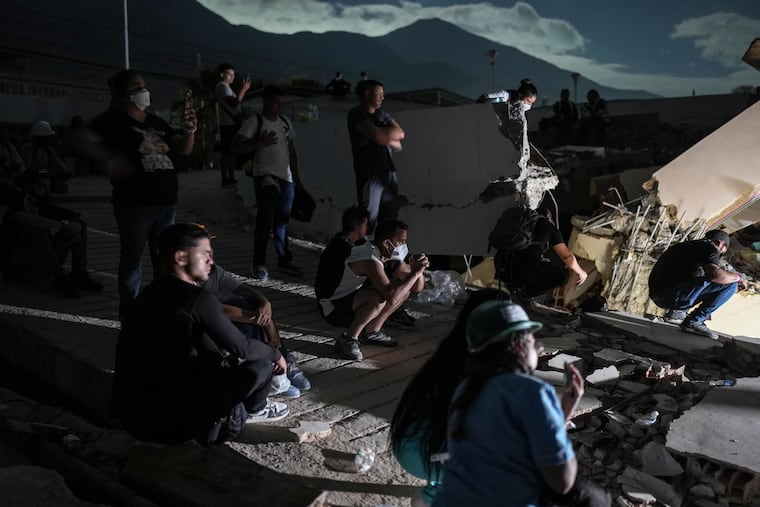 Residents watch rescuers' efforts to reach survivors early Monday beneath the rubble of a building that collapsed in the earthquakes in La Guaira, Venezuela.