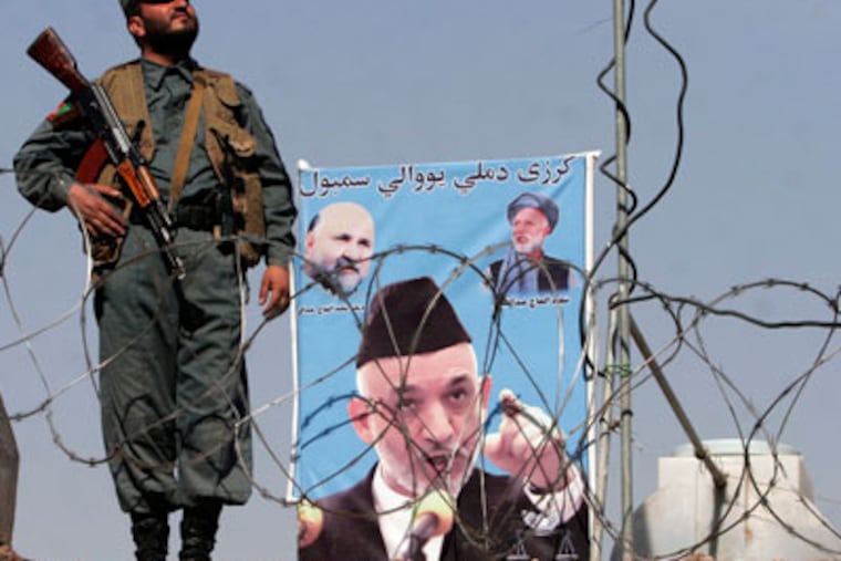 An Afghan police officer stands guard next to a poster showing President Hamid Karzai in Jalalabad, Nangarhar province, east of Kabul, Afghanistan. (AP Photo/Rahmat Gul)