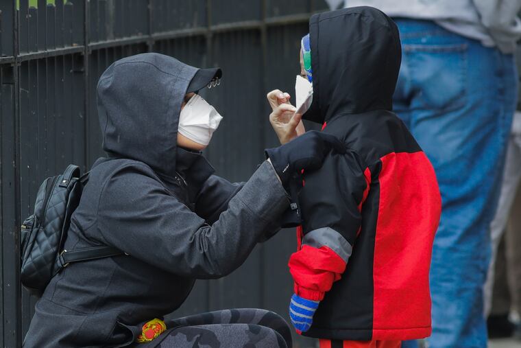 A woman adjusts her child's protective mask as they wait in line to be screened for COVID-19 at Gotham Health East New York, Thursday, April 23, 2020, in Brooklyn.