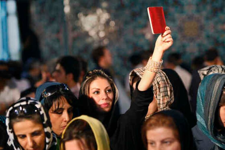 An Iranian woman holds her identity card aloft as she waits in line to cast her vote at the Ershad mosquein northeastern Tehran. A long day of voting featured blistering heat and nighttime downpours.