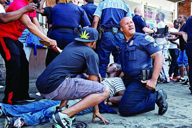 A man lies on a Baltimore sidewalk as officers attempt to calm the crowd. The man was taken to a hospital but was not injured, police say.