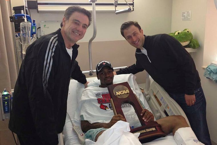 Louisville's Kevin Ware holds the Midwest Regional trophy in a hospital bed. Coach Rick Pitino (left) and Pitino's son, Richard, presented the hardware.