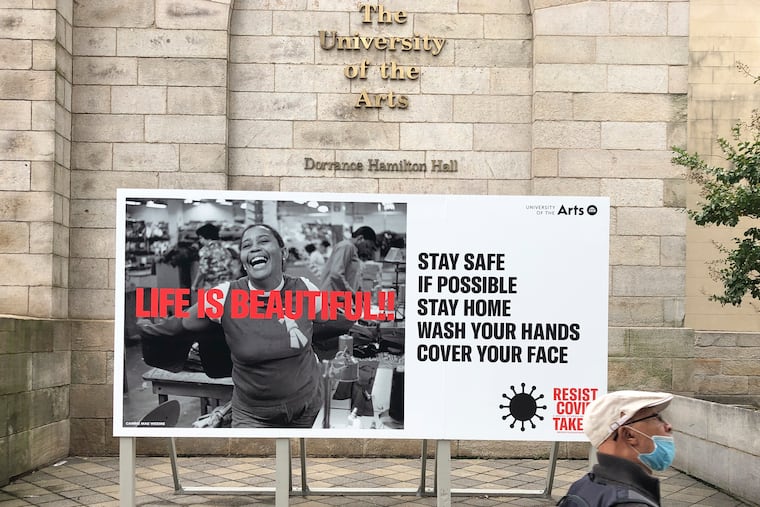 A pedestrian walks past a COVID-19 billboard in front of the University of Arts in Center City on Wednesday, October 21, 2020.