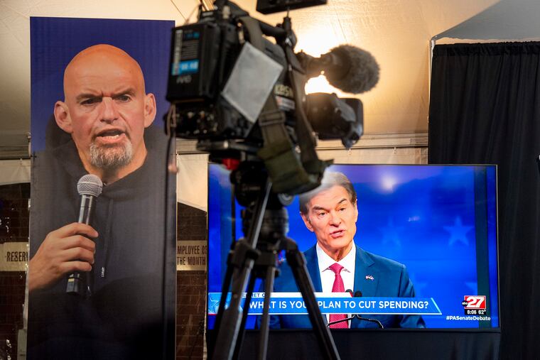 Republican Mehmet Oz (right) is seen live on a monitor in the media tent, next to a poster of Democrat John Fetterman as the two U.S. Senate candidates held their first and only debate Tuesday in Harrisburg.