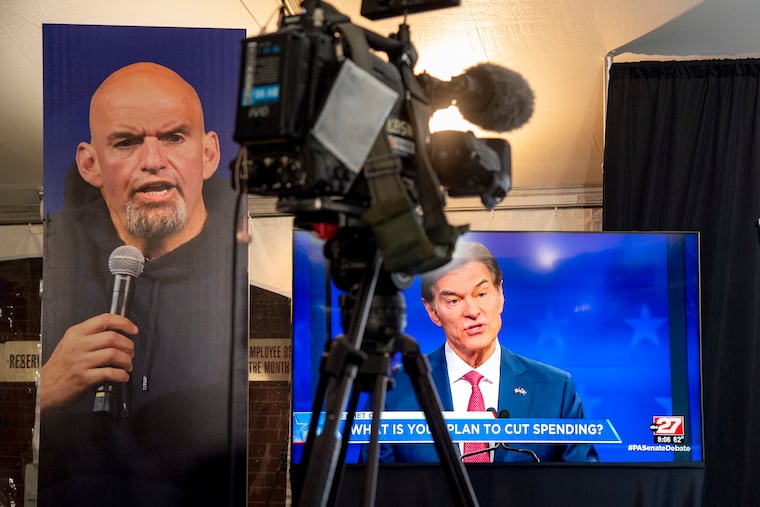 Republican Mehmet Oz is seen live on a monitor in the media tent, next to a poster of Democrat John Fetterman (left).