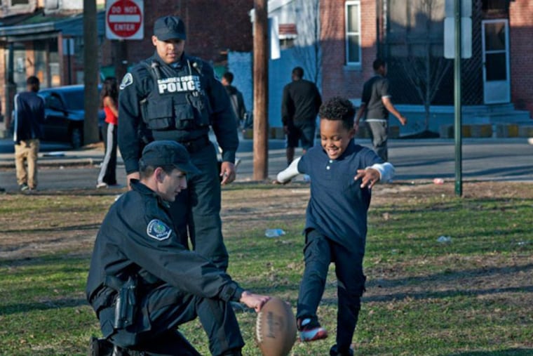 Camden County police officers Oliver Isshak (foreground) and Nicholas Voorhees played football with kids yesterday, April 1, 2014, in Camden's Whitman Park.
