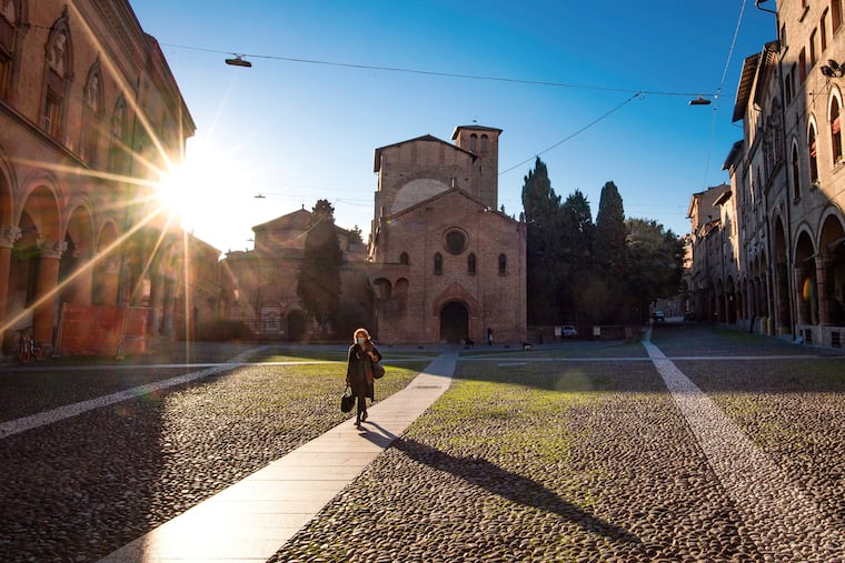 A woman walks past the Basilica of Santo Stefano, in Bologna, Italy, Wednesday, March 11, 2020. In Italy the government extended a coronavirus containment order previously limited to the country’s north to the rest of the country beginning Tuesday, with soldiers and police enforcing bans. For most people, the new coronavirus causes only mild or moderate symptoms, such as fever and cough. For some, especially older adults and people with existing health problems, it can cause more severe illness, including pneumonia.
