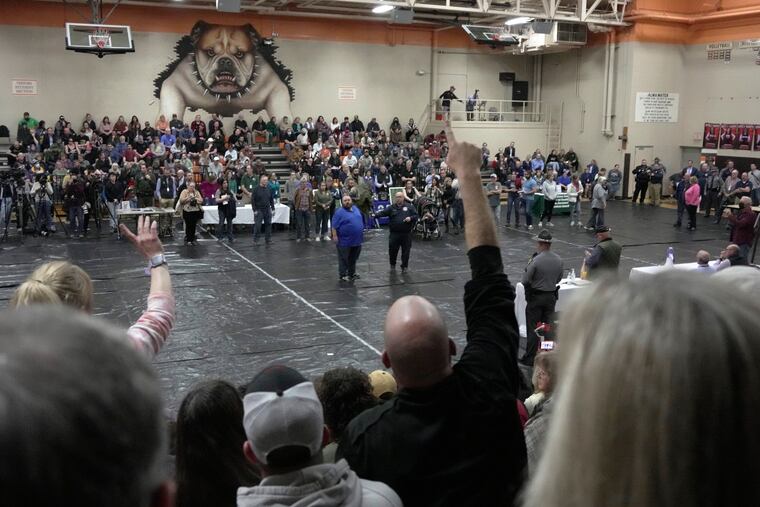 A man raises his hand with a question for East Palestine Mayor Trent Conaway (center) during a town hall meeting Wednesday night.