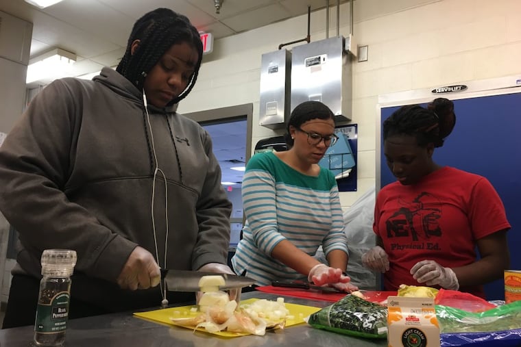 Jasmine Mitchell (left) chops onions and Delaney Taylor (center) demonstrates how to smash a clove of garlic as Destiny Crawford looks on.