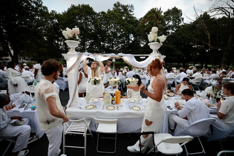 Zach Lutz (left) of Philly created this setup for his table. Annie Rulli of Haddon Twp., (center) estimates she has been to 10 Dîner en Blanc events. Jess Flamm of Philadelphia joins them for the 11th Dîner en Blanc at Memorial Hall in Fairmont Park in Philadelphia on Thursday, Aug. 10, 2023.
