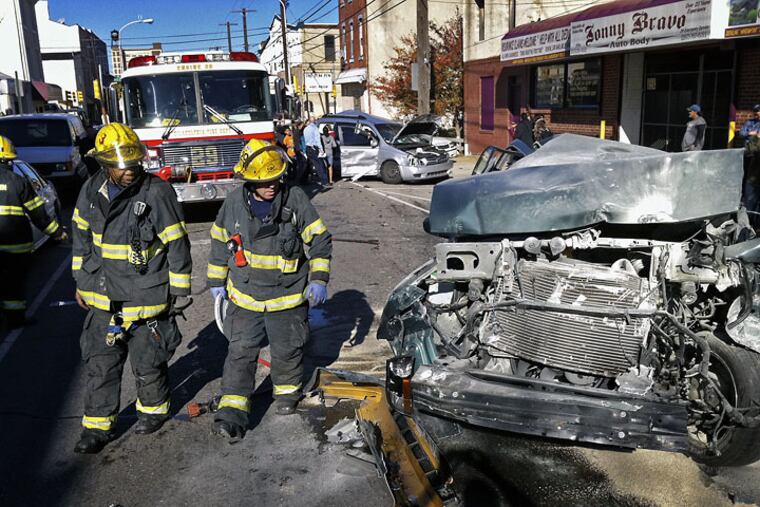 Firefighters walk by one of the cars damaged in a severe multi-car accident at the intersection of Cecil B. Moore Avenue and North Second Street at 1 p.m. Thursday.