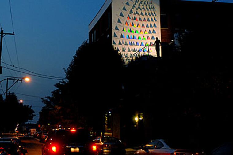 Ray King is just a small shadow as he poses on rooftop deck of in his Northern Liberties home. The new installation on the outside wall of his studio is a gift to his neighborhood. (Tom Gralish / Inquirer)