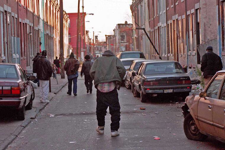 A group of men (center) walk down Darien Street near the Fairhill Cemetery after police chased them out of a vacant house that had been used as a shooting gallery.