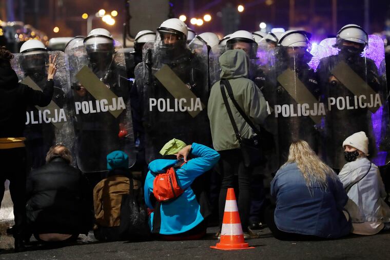 A police cordon guards the house of Poland's ruling conservative party leader Jaroslaw Kaczynski against a crowd protesting a decision by the Constitutional Court, in Warsaw, Poland.