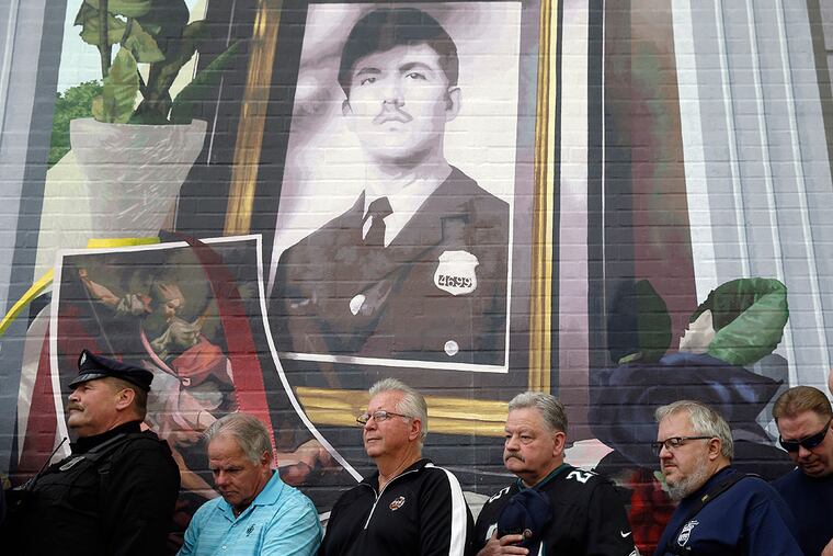 Former coworkers of slain Philadelphia police officer Daniel Faulkner stand beneath a new mural of him Monday, Nov. 24, 2014, in Philadelphia. The mural is painted on the side of the police station Faulkner worked at in the Chinatown section of the city. Daniel Faulkner was shot to death by Mumia Abu-Jamal on a downtown street in 1981. (AP Photo/Matt Rourke)
