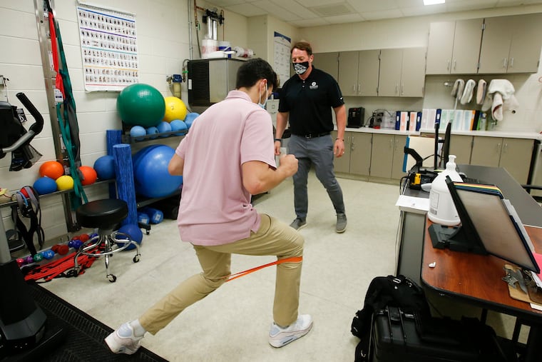 Lower Merion High School trainer Jason Luty (right) watches senior basketball player Zack Wong use an exercise band in the school's training room on June 4, 2021. Wong, who is graduating, was a forward on the basketball team.
