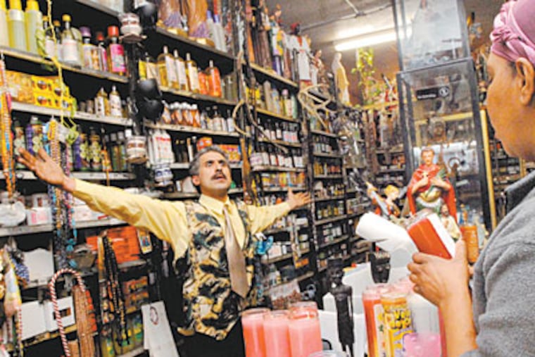 Angel Perez, who runs Botanica Maria in the city’s Fairhill neighborhood, talks about his goods as a customer ponders a purchase. (APRIL SAUL / Staff Photographer)