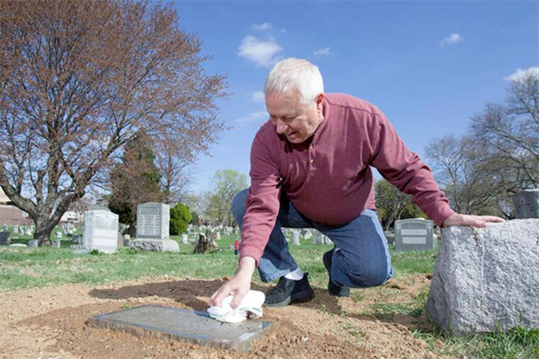 John DeVos cleans off his brother Michel's recently reset burial stone at Greenmount Cemetery.