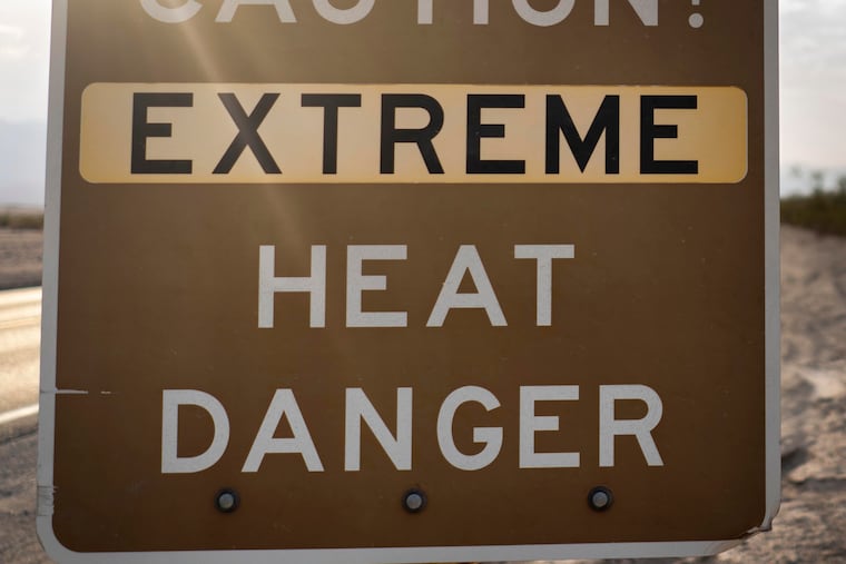 With the Amargosa Mountain Range in the background at sunrise, a sign warns park visitors of "extreme heat danger" along Highway 190.