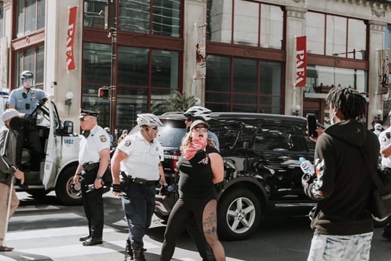 Philadelphia police Staff Inspector Joseph Bolonga, left, watches Shoshana Akins, in pink bandanna, as she is detained by police at a protest last Monday. Akins said Bologna twisted her fingers, to the point she feared they would break, while she was detained and in handcuffs.