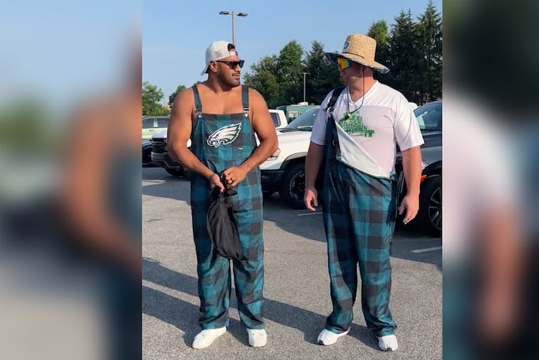 Eagles Jordan Mailata (left) and Landon Dickerson sporting Eagles bib overalls as they arrive at training camp Tuesday.
