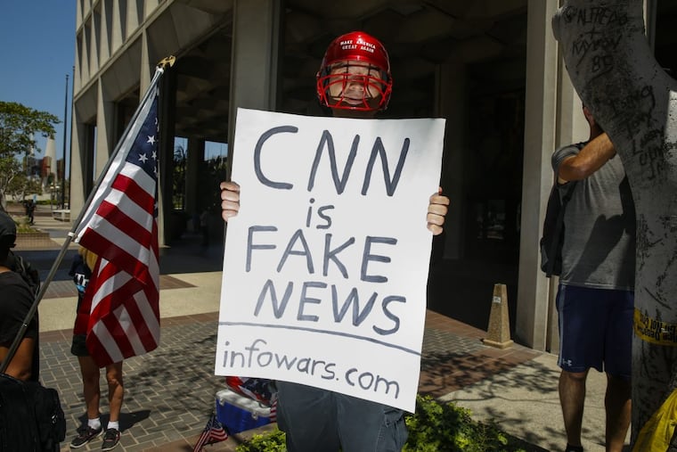 A man holding a sign that says, "CNN is Fake News" and "infowars.com" positioned himself into photos while the media covered an Impeachment March in downtown Los Angeles on July 2, 2017.