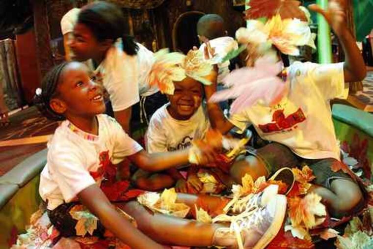 Girls play with falling leaves in the "autumn" section of the "Exploring Trees Inside and Out" exhibit at Please Touch Museum.