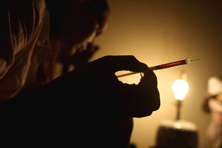 Holding a syringe filled with black tar heroin, an addict searches for a vein in her leg to inject herself . (Gina Ferazzi/Los Angeles Times/MCT)