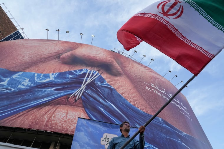 A man waves an Iranian flag for a pro-government campaign under a billboard with graphic showing Strait of Hormuz and sewn lips of President Donald Trump in a square in downtown Tehran, Iran, on Wednesday.