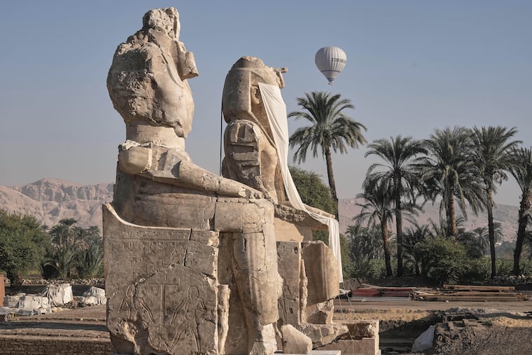A hot air ballon flys over the assembly of two giant alabaster statues of Pharoah Amenhotep III, before the official opening, in the southern city of Luxor, Egypt, Sunday, Dec. 14, 2025.