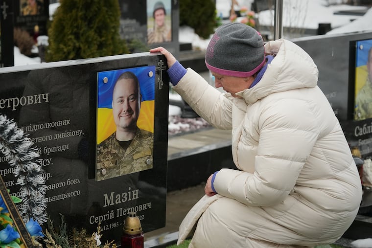 A woman sits in front of her relative's grave during a memorial service in Bucha for fallen Ukrainian soldiers on the fourth anniversary of the Russian invasion of Ukraine.