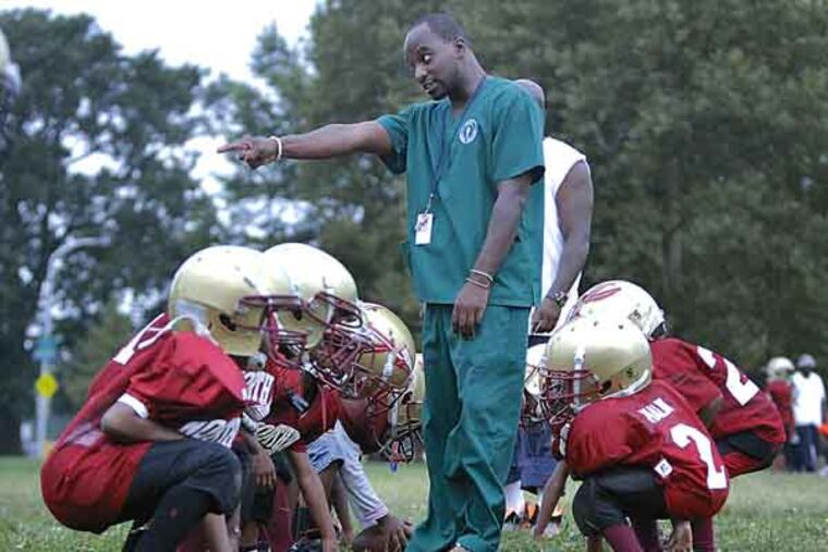 North Philly Aztecs 75 lb coach Roling Davis works with the 4,5 and 6 yr olds during practice in Hunting Park on Aug. 7, 2013. The teams will soon be playing on the nearly completed $1.4 million dollar Team Vick Field in Hunting Park. ( ELIZABETH ROBERTSON / Staff Photographer )