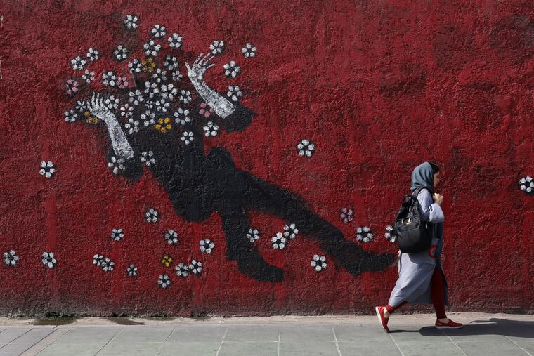 A woman walks past a mural in a sidewalk in downtown Tehran, Iran, on Sunday.