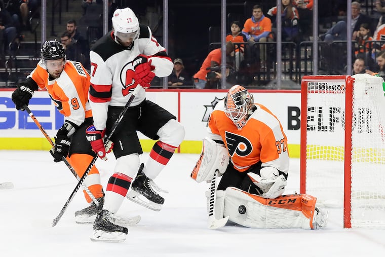 Flyers goaltender Brian Elliott stops the puck while Ivan Provorov (left) and New Jersey's Wayne Simmonds battle in front during a game last season.