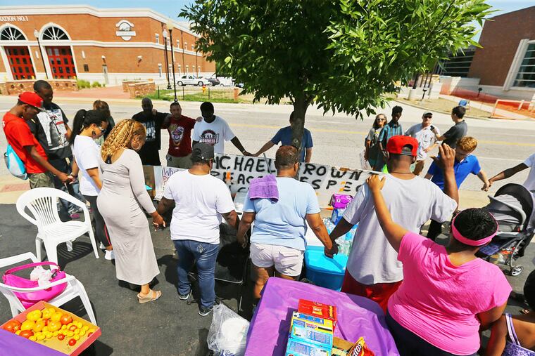 A small group of protesters join hands and bow their heads for a prayer across the street from the police department on Tuesday, Aug. 19, 2014, in Ferguson, Mo. After nine days of unrest following the fatal police shooting of Michael Brown, an unarmed 18-year-old black man, law enforcement and political leaders are looking for ways to restore peace to the community. (AP Photo/Atlanta Journal-Constitution, Curtis Compton)