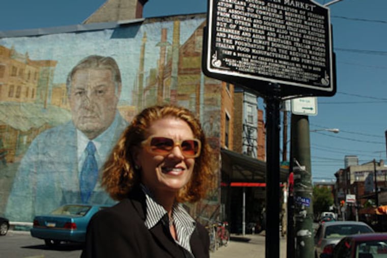Celeste Morello poses on South 9th Street near a new marker commemorating the Italian Market. She designed the marker. A book she authored - "The Philadelphia Italian Market Cookbook: The Taste of South 9th Street," was sold down the street until recently. (Sarah J. Glover / Inquirer)