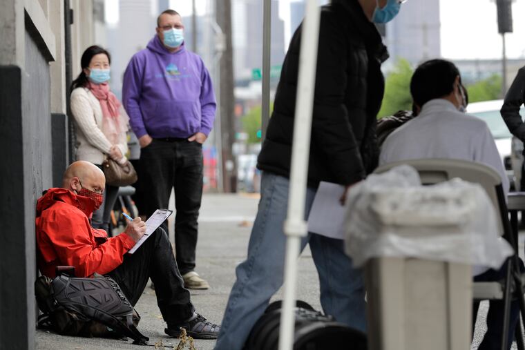 Glen Buhlmann, lower left, fills out a job application during a walk- and drive-up job fair in Seattle for clothing maker Outdoor Research's new line of face masks and other personal protection equipment the company has started manufacturing due to the coronavirus pandemic.