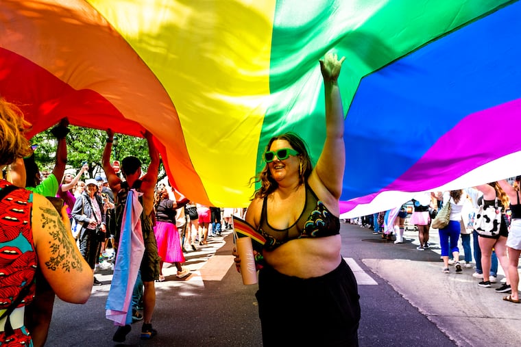 Niki Daker of South Philadelphia climbs under the 200 foot long Pride flag as it makes its way along Walnut street among the thousands of people celebrating queerness and the start of Pride Month at the Pride March and Festival in Center City Sunday, June 4, 2023.