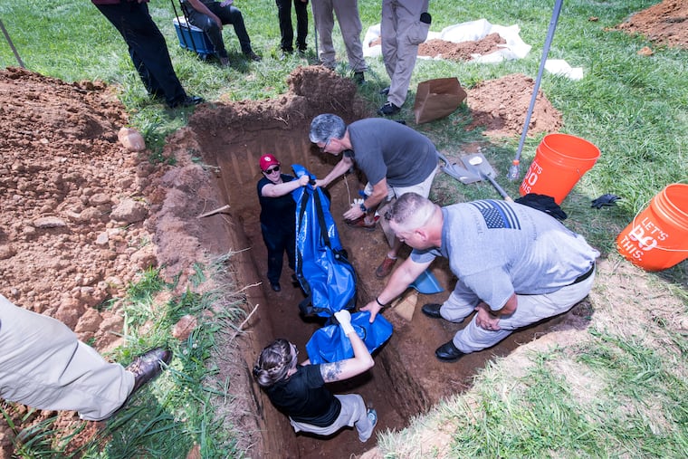 Kristen Verostick, University of South Florida Department of Anthropology, right, and Jamie Willer, Philadelphia Medical Examiners Office, hand a body bag containing the body of a white male, estimated to be 18-21 years of age, found floating in a creek at Lewis and Richmond Streets. The male had been stabbed multiple times and his body was weighted down with weights that were chained to his feet and legs. The manner of death was ruled homicide. The exhumation of the body took place at 12898 Dunk Ferry Road.