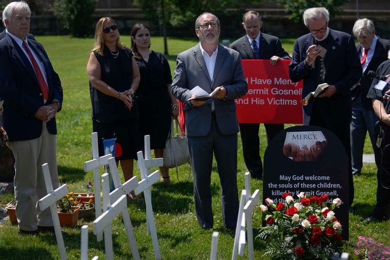 BEN MIKESELL / STAFF PHOTOGRAPHER The Rev. Patrick Mahoney leads a prayer (above) at the unmarked grave site at Laurel Hill Cemetery. David Walsh, 70, (at right) carries a box of roses for the memorial service for Kermit Gosnell's victims.
