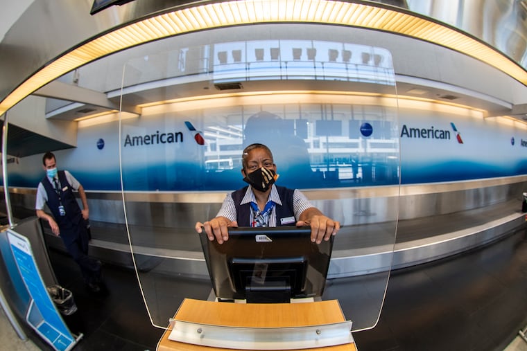 American Airlines employee, Chan Medley stands behind a safety shield to remind guests to practice physical distancing at the Philadelphia International Airport, in Philadelphia, Pa. Tuesday, May 26, 2020.