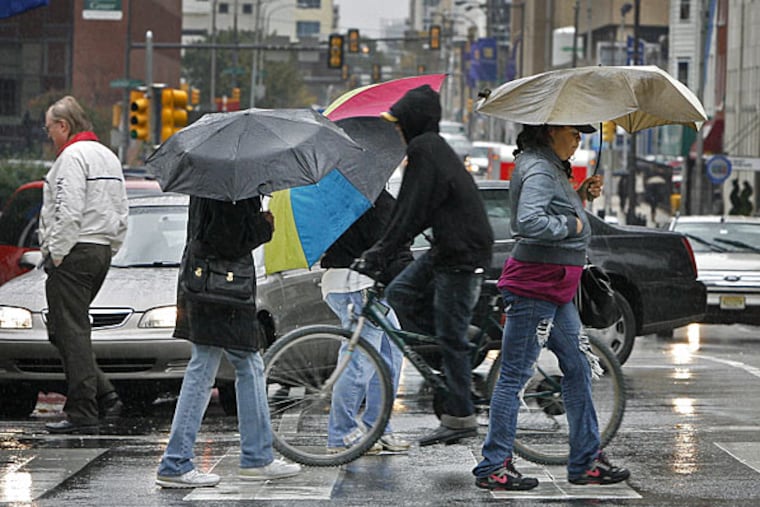 Pedestrians cross 15th Street in Center City with umbrellas to protect them from the rain.