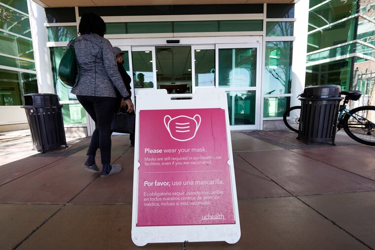 A sign advising visitors to don face coverings stands outside the main entrance to UCHealth University of Colorado hospital Friday, April 1, 2022, in Aurora, Colo. COVID cases are starting to rise again in the United States, with numbers up in most states and up steeply in several. One expert says he expects more of a “bump” than the monstrous surge of the first omicron wave, but another says it’s unclear how high the curve will rise and it may be more like a hill.