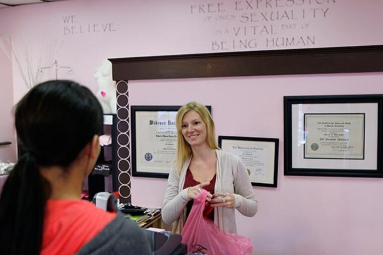 Jill McDevitt rings up a sale of liquidation items at "Feminique," her store in West Chester in the last hour before the final closing Sunday, November 10, 2013. On the wall behind her are her undergratuate, masters, and doctorate degrees in human sexuality. ( MICHAEL S. WIRTZ / Staff Photographer )