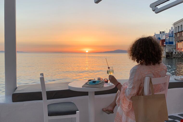 A visitor watches the sunset at a bar in an area known as Little Venice in the main town of the island of Mykonos, Greece. Business owners and locals officials on the Greek holiday island of Mykonos, a popular vacation spot for celebrities, club-goers, and high rollers, say they are keen to reopen for business despite the risks of COVID-19 posed by international travel. Greece will official launch its tourism season Monday, June 15, 2020 after keeping the country's infection rate low.