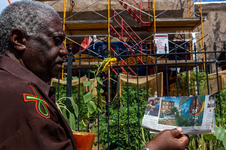 Ancestor Gold Sky holds a picture of a garden memorial in honor of a young black girl was starved by her mother in the 1990s. The mural featuring the little girl's face has been covered by a new mural on the Harper Street Garden walls.