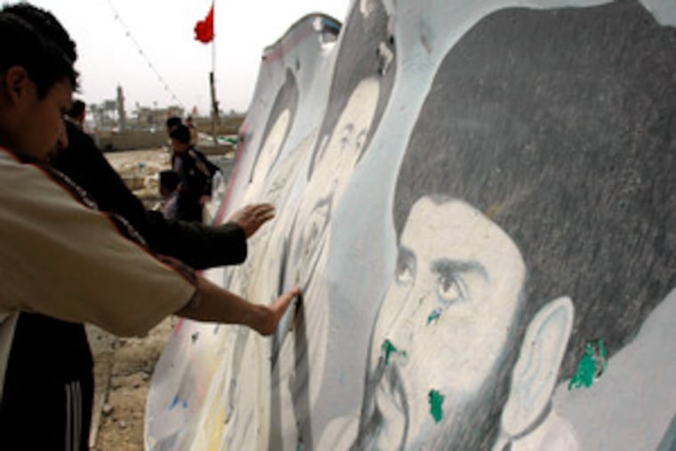 People touch a damaged poster of Muqtada al-Sadr (right) and the late Mohammed Baqir al-Sadr at a mosque in Haswa, where a suicide bomber killed 11 last week.